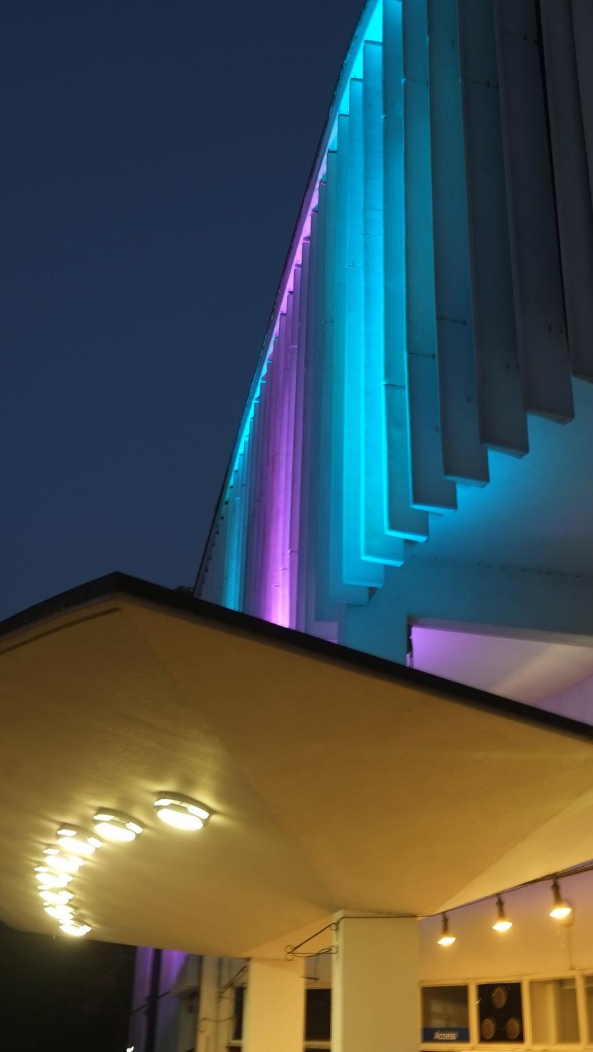 Photo of the front of the theatre at night, lit up in purple and blue. 