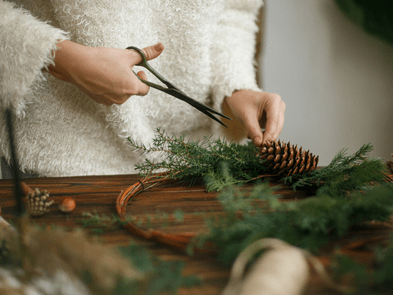 A person wearing a fluffy jumper cutting a wreath with scissors
