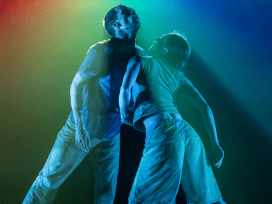 2 dancers chest to chest with rainbow lights