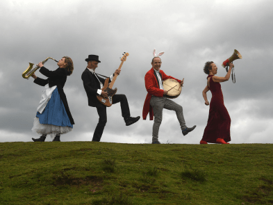 4 actors with various instruments on a hill