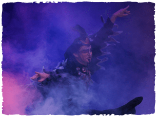 A performer in a black feathered outfit dances in pink mist