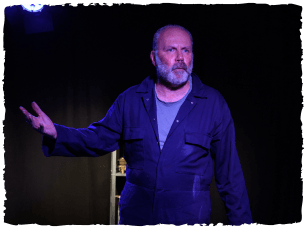 Richard Vergette wearing a blue jacket and grey tshirt points to his right 