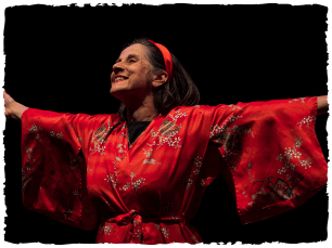 Lady in satin red dressing gown, with matching headband, with arms out to side, smiling wide!