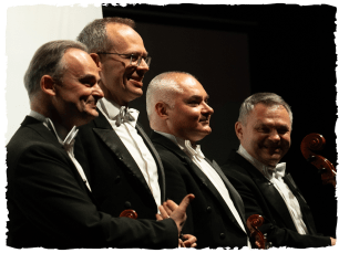 4 men in suits smiling, facing audience
