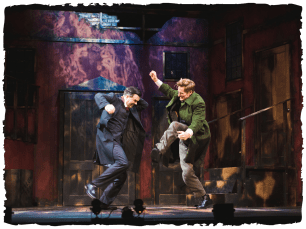 two men - one in a green jacket the other in a dark suite, fighting against a backdrop of old buildings