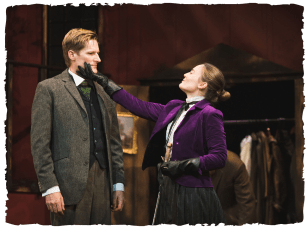 A woman with a purple velvet jacket holding the face of a man in a tweed suit