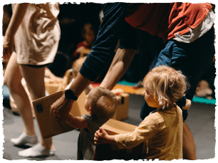 Little girl walking with help of adult, holding big box