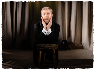 man in black suit, holding hands up to face as if shockd