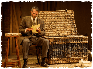 an actor sitting on a chair next to a small table reading a letter