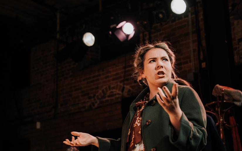 Image of a young woman on stage performing under stage lights.