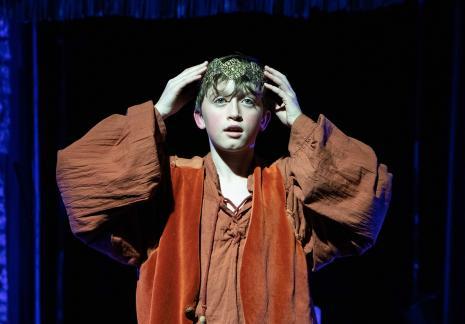 A young male in costume putting on a crown.