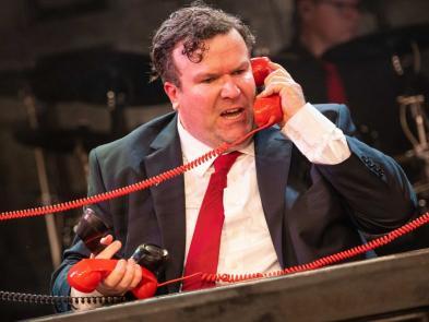 Performer in suit and red tie comedically picking up multiple phones at once