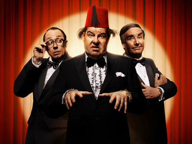 Tommy Cooper, Eric Morecambe and Bob Monkhouse impersonators  in front of a red camera