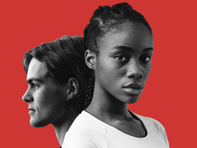 A man looks out left and a woman looks towards the camera in black and white in front of a red background