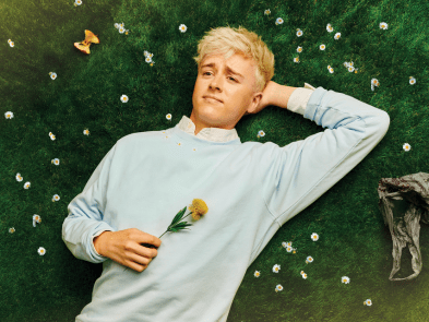A man lying in some grass holding a flower