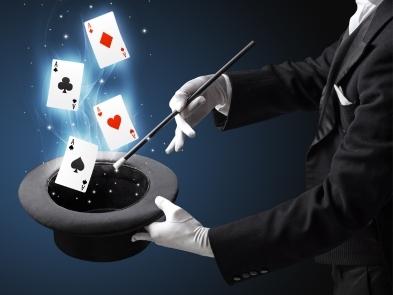 Man with magic wand holding an upside down top hat with playing cards hovering above