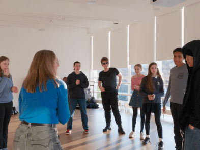 a group of young people and 2 group leaders stood in a circle playing a game